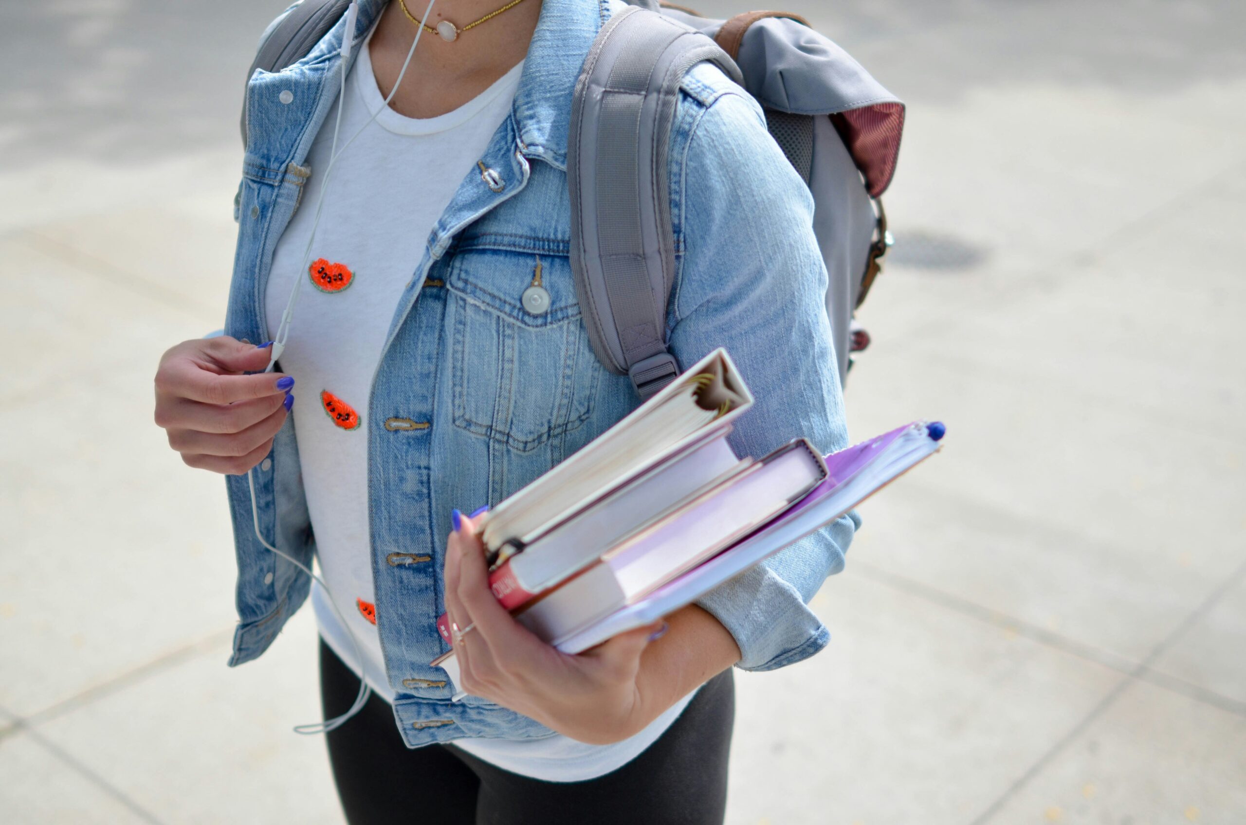 A student wearing their backpack and carrying textbooks and notepads for class