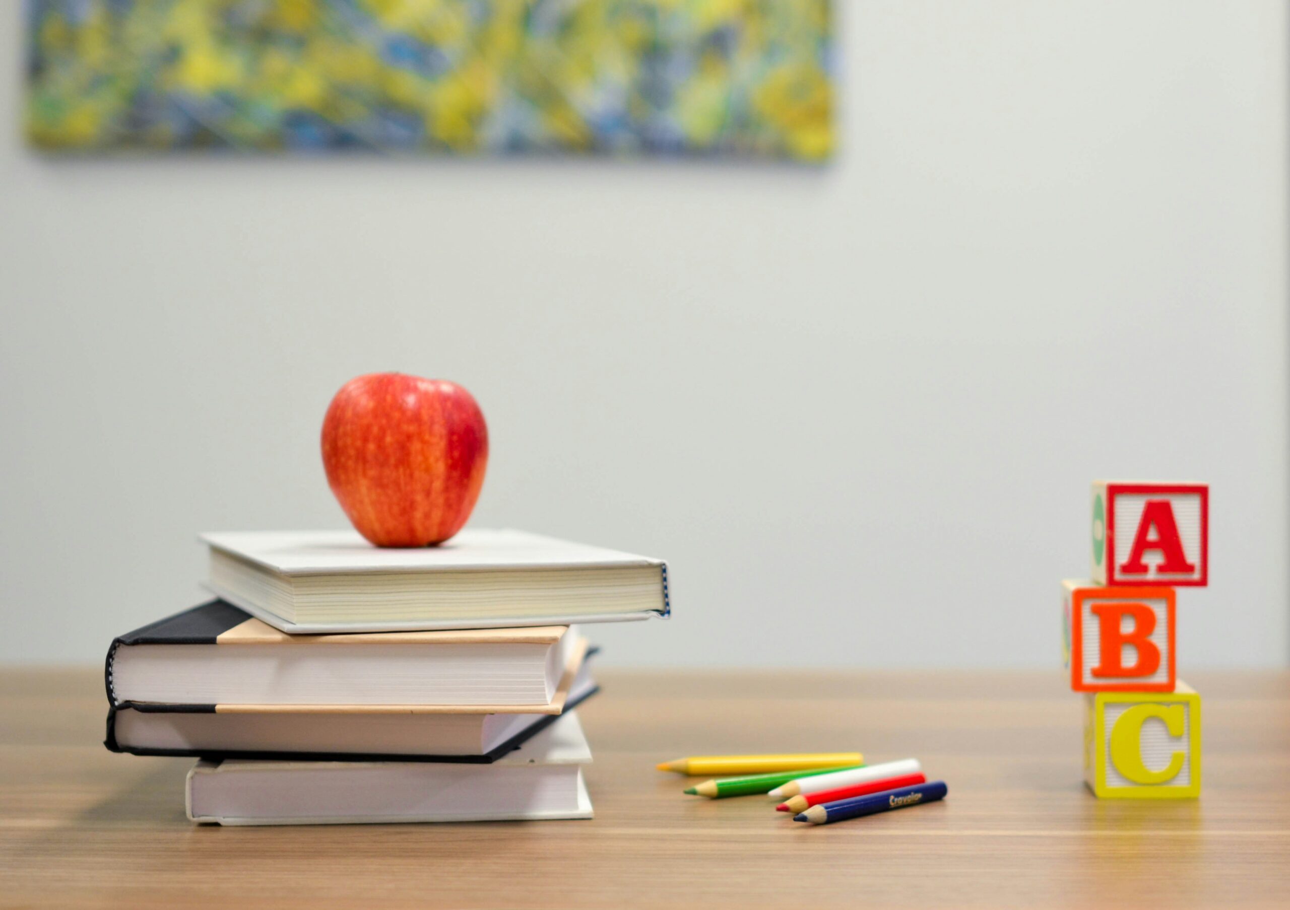 A desk with books, an apple, colored pencils, and children's blocks sitting on top of it