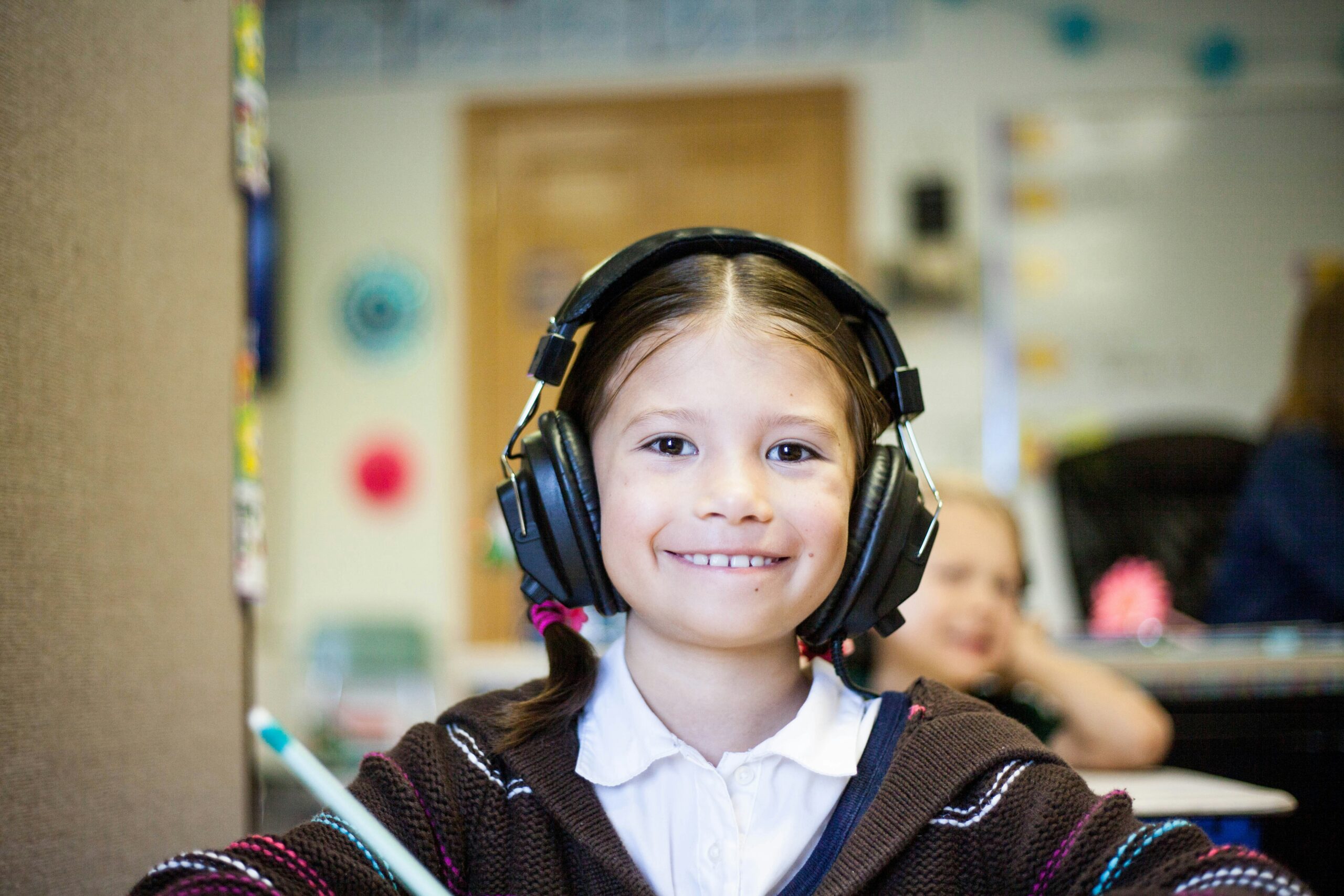 A young student with headphones on in the classroom smiling at the camera